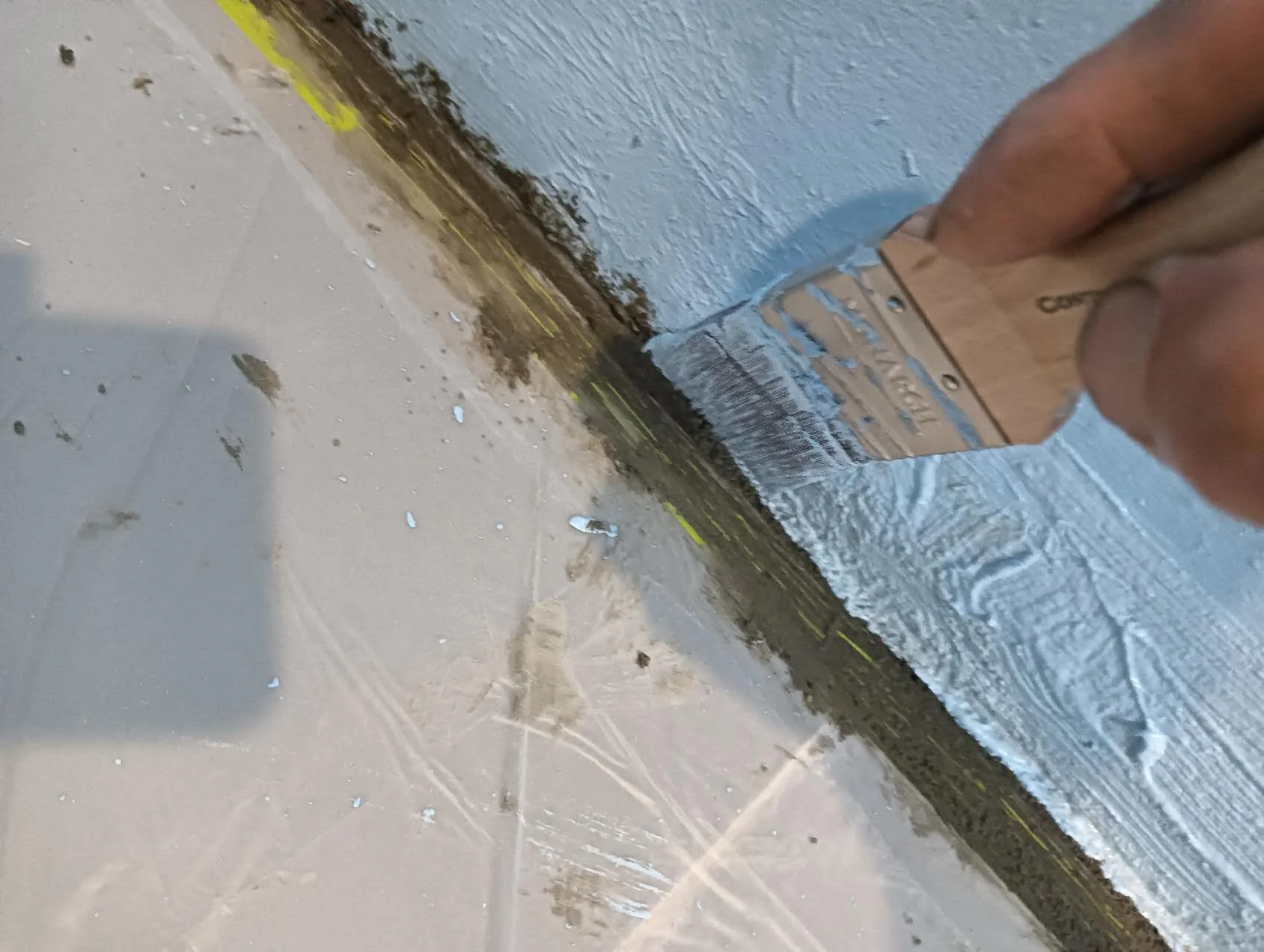 Brush applying blue coating along a shower wall base beside a protected floor