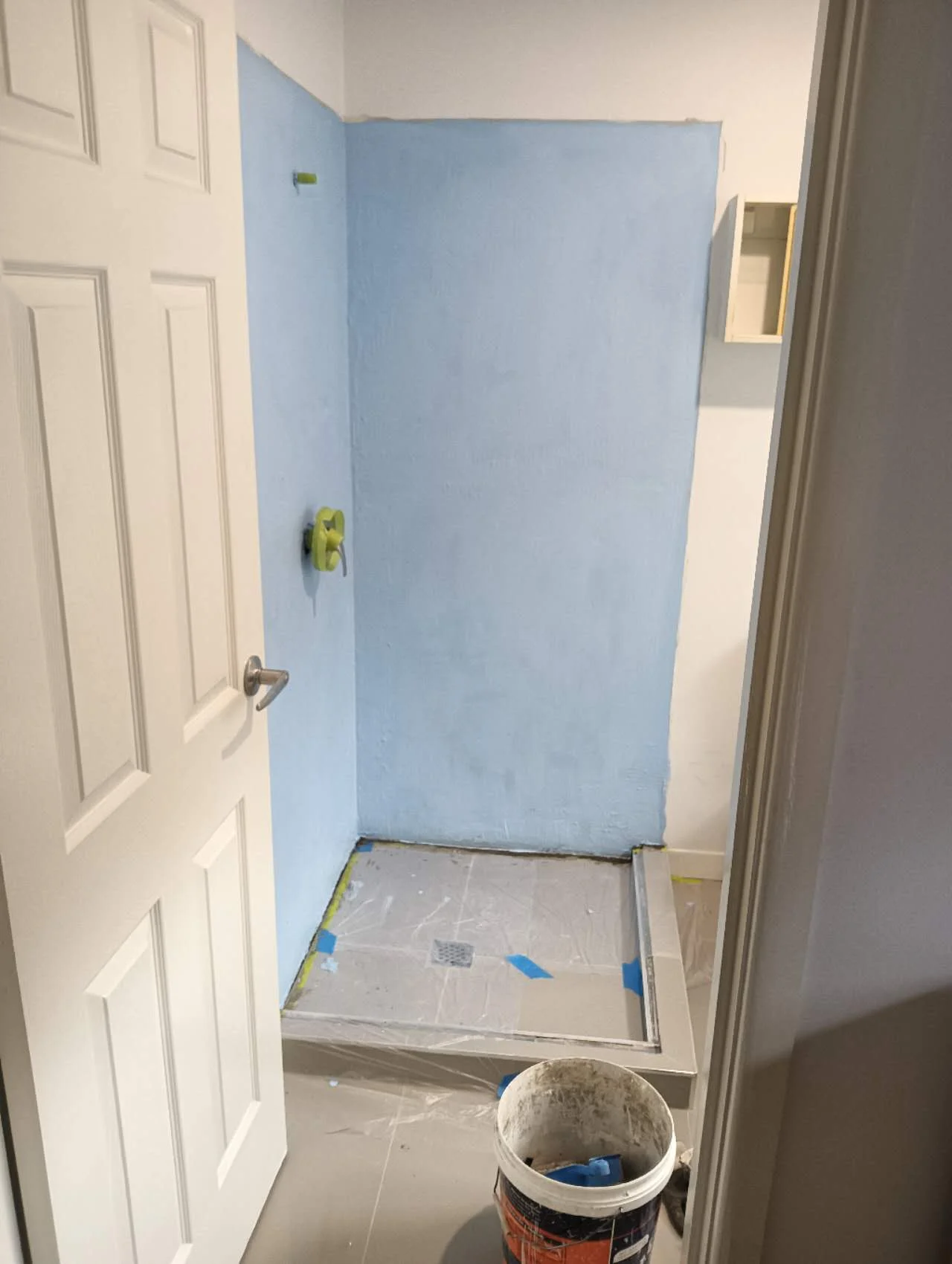 Blue-coated shower walls with masked fittings and the existing floor protected