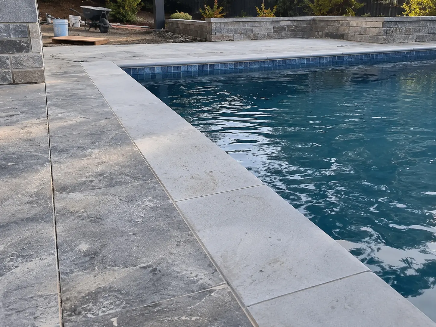 Grey pool surround tiles and pale coping along the edge of a swimming pool
