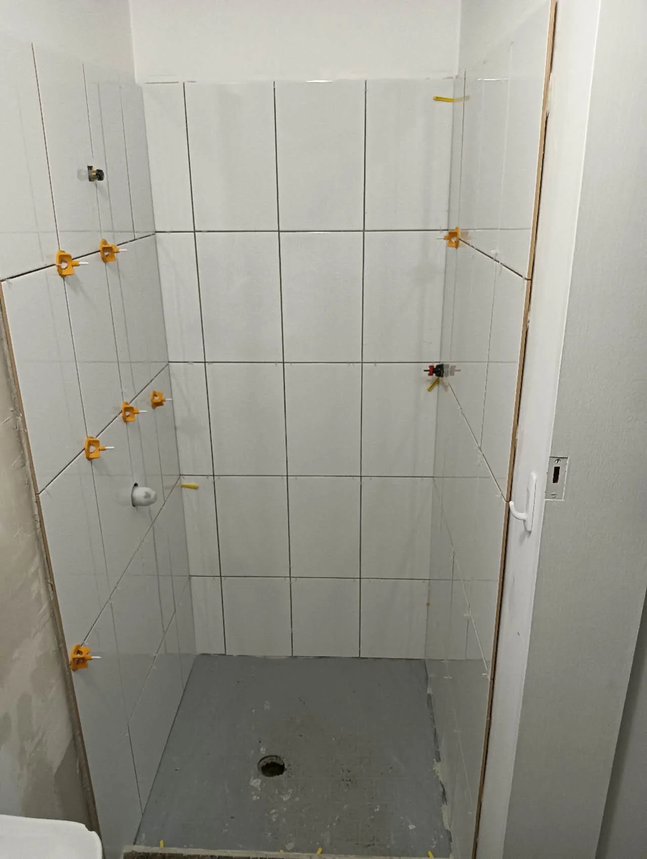 Shower wall tiles during installation with levelling clips and an unfinished floor