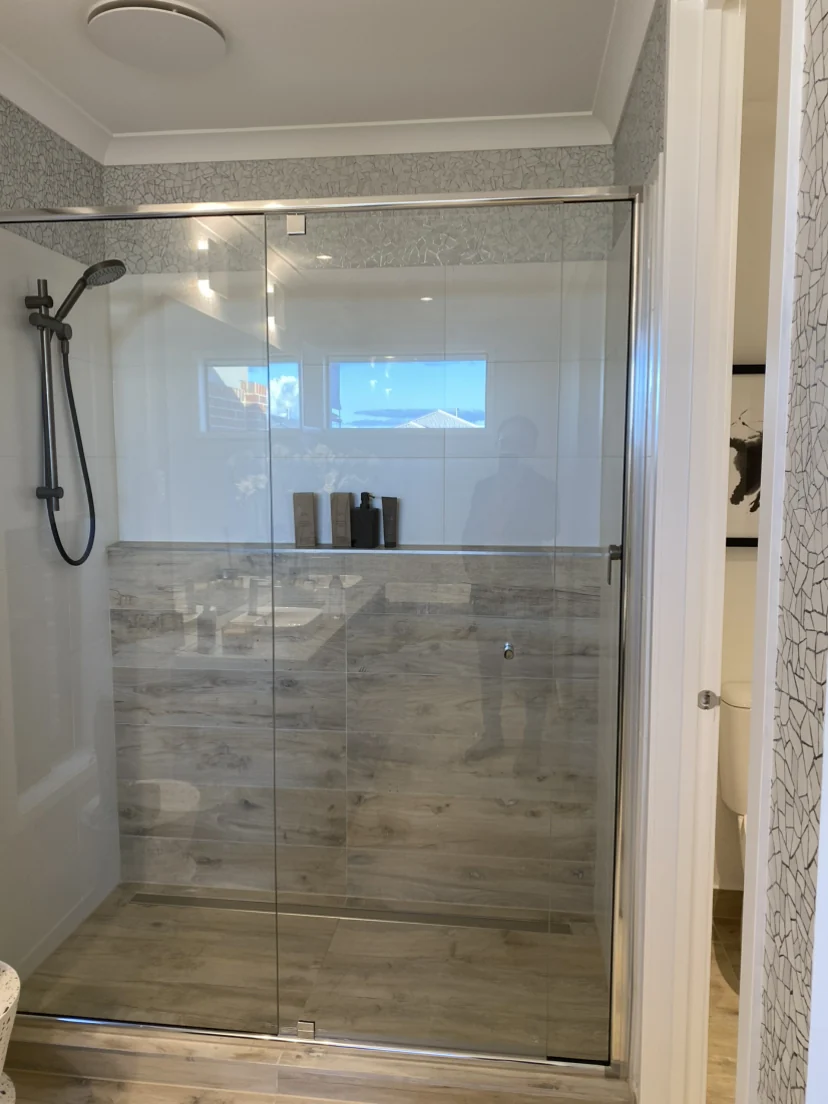 Grey-brown timber-look porcelain tiles on a shower floor and lower wall behind a glass screen, with white upper wall tiles