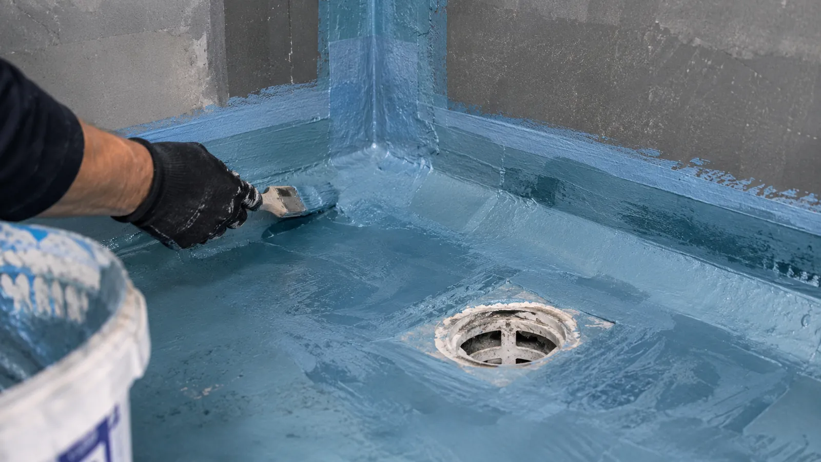 Waterproofing being detailed around a floor drain and wall-floor junction